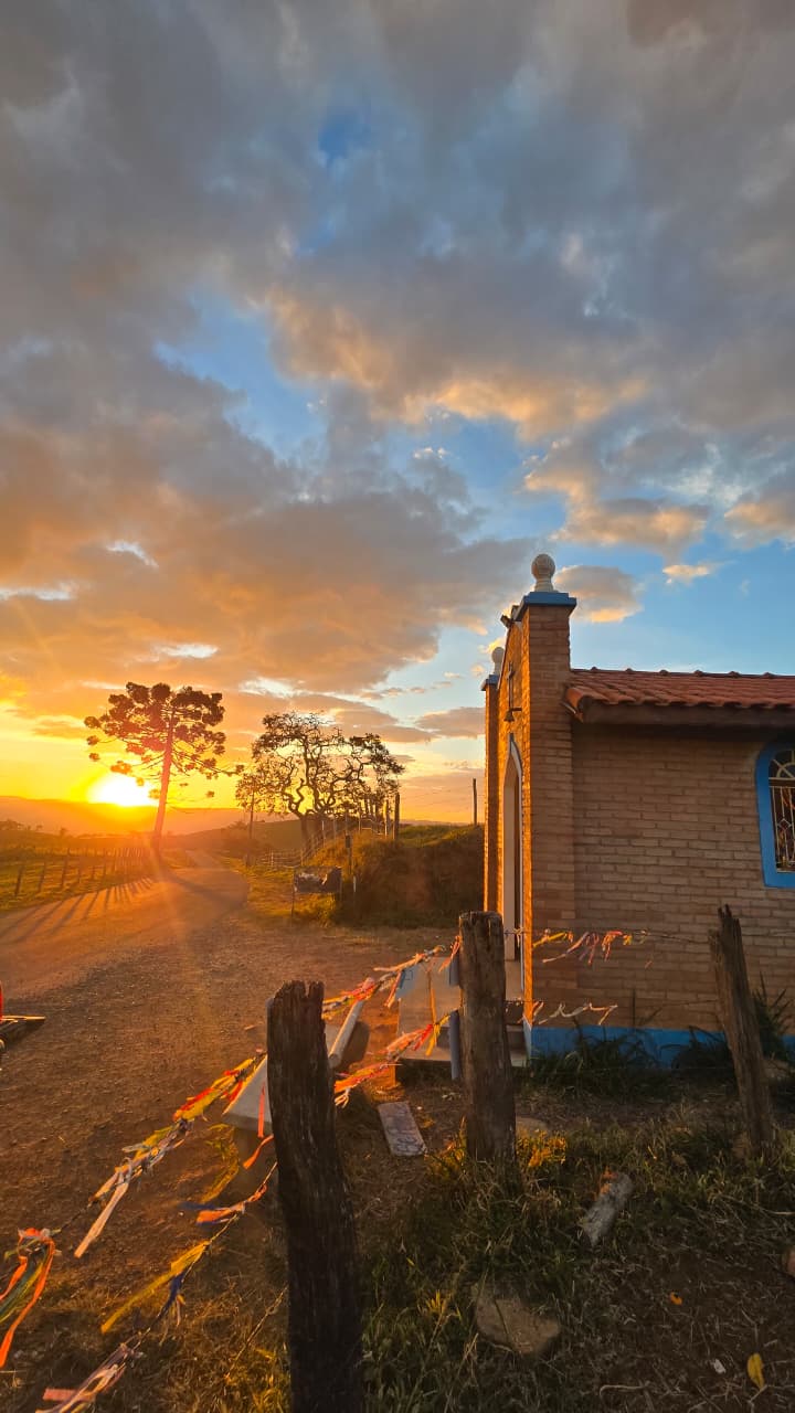 Capela de tijolos à beira de estrada de terra no pôr do sol, com bandeirinhas coloridas